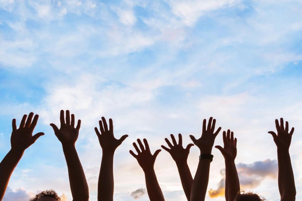 4 peoples hands reaching to the sky.